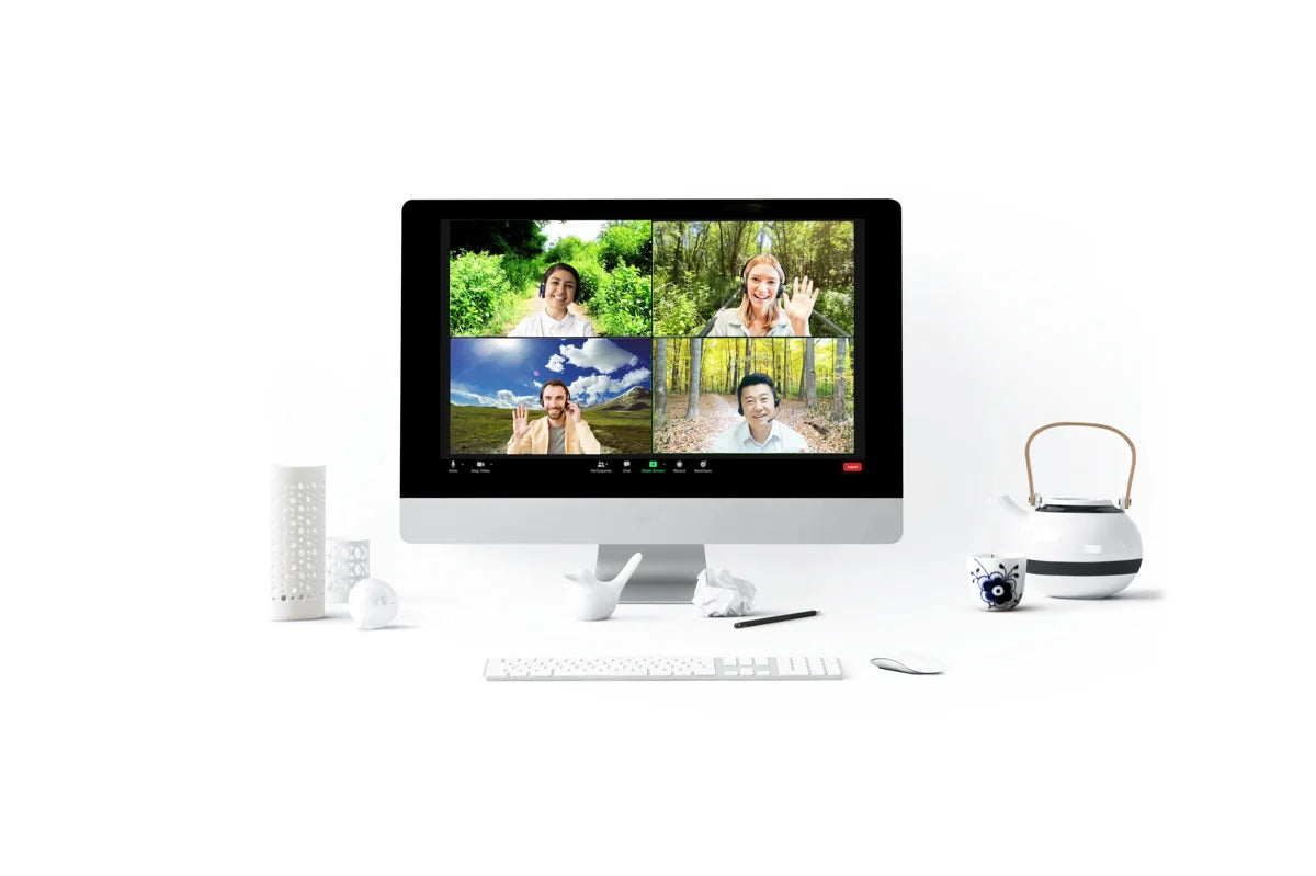 A computer screen shows a video call with four people, each in different nature settings. The desk has a keyboard, mouse, tissue, teapot, and other small items, all on a white background.