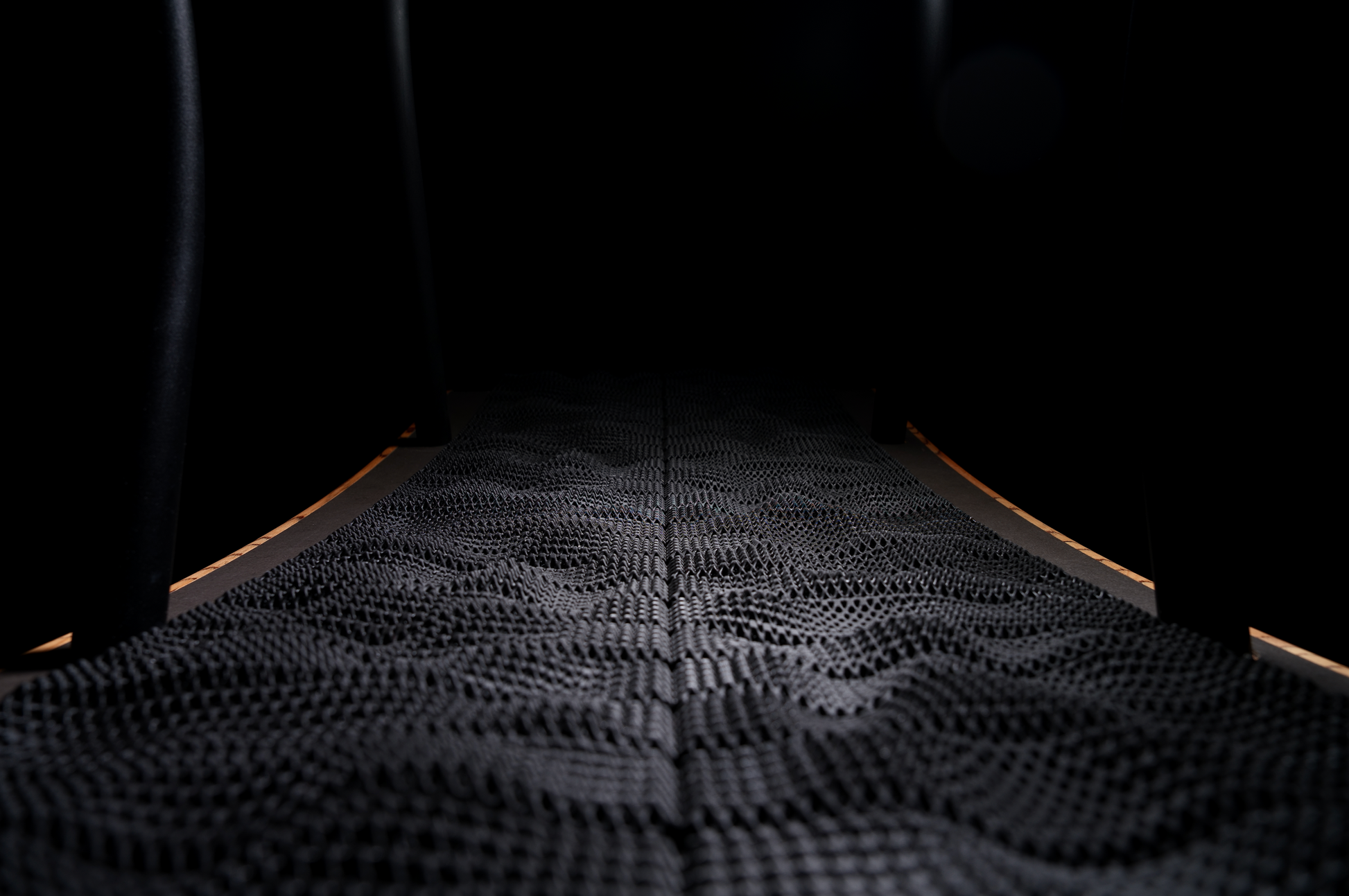 Close-up of the TheraFloor® Home Upgrade-Kit for Walkolution 1: a wavy, textured black surface with fine geometric patterns, softly lit curved edges, and shadowed surroundings—resembling a cushioned treadmill mat.