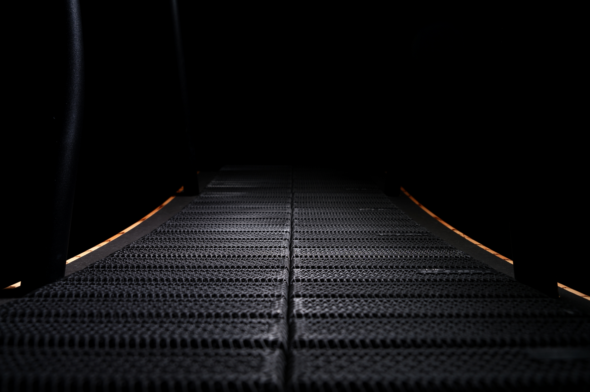 A close-up view of the TheraFloor® Home Upgrade-Kit for Walkolution 1 shows its dark, textured surface under minimal lighting, emphasizing the mat’s durable edges and cushioning as it fades into the background.