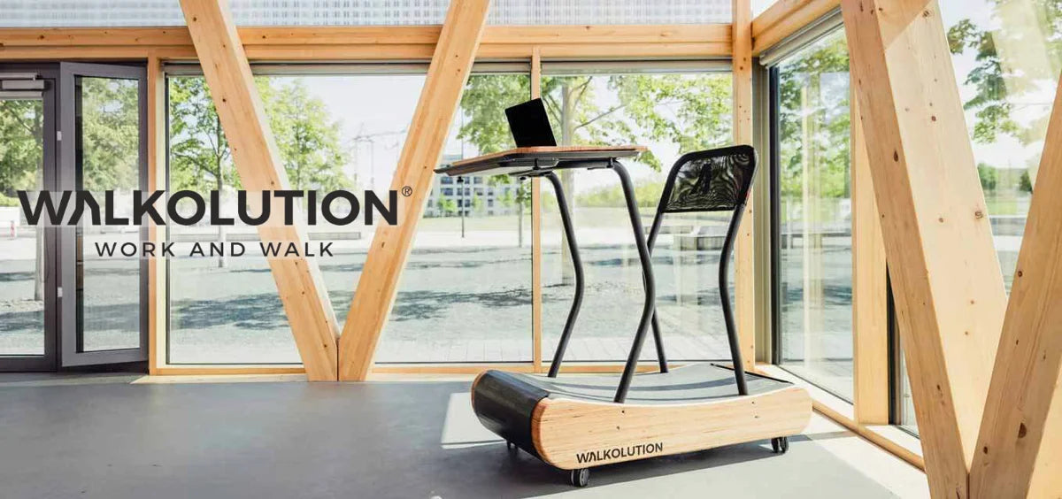 A wooden treadmill desk with a black chair and laptop is positioned in a bright, modern room with large windows and wooden beams. The words “WALKOLUTION WORK AND WALK” are displayed on the left.