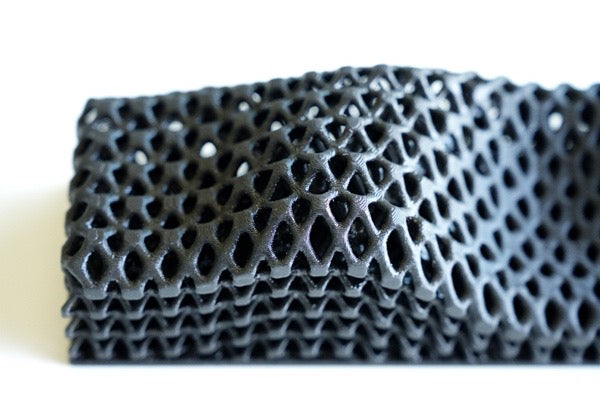 Close-up of the All Surfaces Sample Box: a black, flexible 3D-printed lattice with a repeating diamond pattern, resembling barefoot-friendly treadmill surfaces, photographed against a white background.