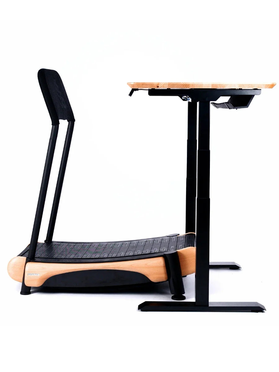 A modern, curved wooden treadmill with a black walking surface sits next to an adjustable-height standing desk with a wooden top and black metal legs.