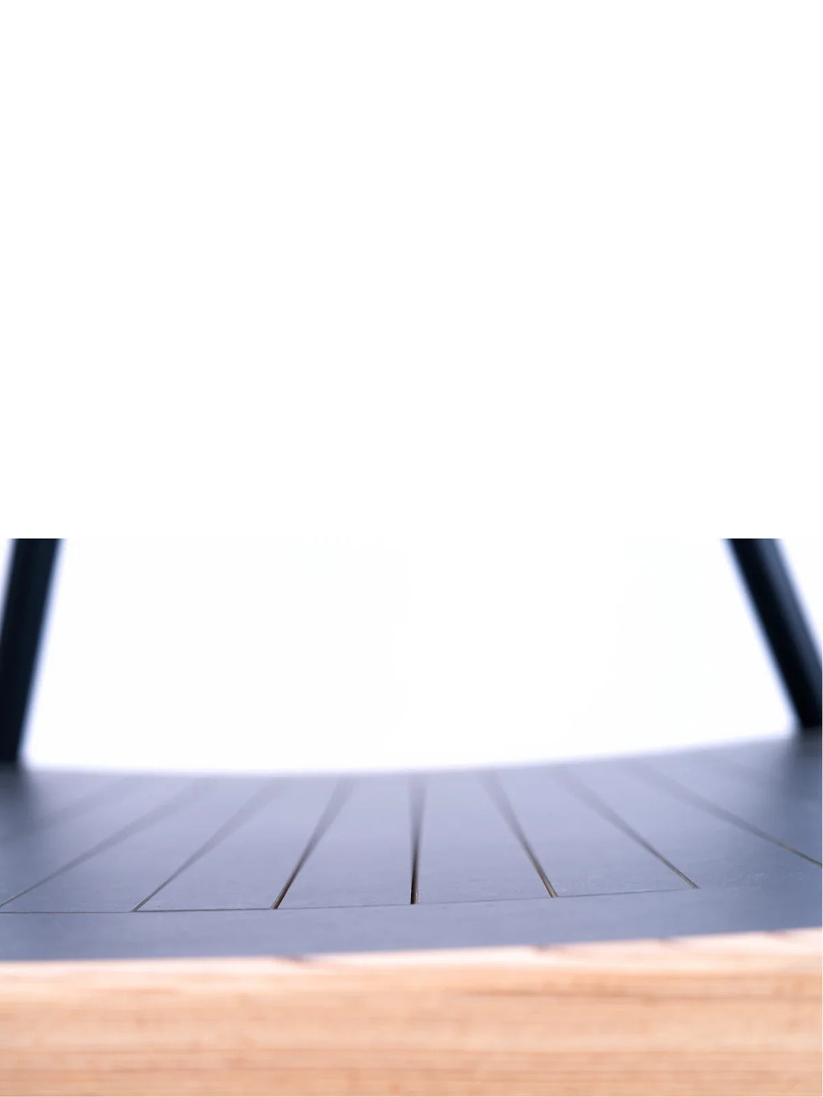 Close-up of the Walkolution 1: a black, curved seat with thin parallel lines and black legs, revealing a light wood layer at the edge. Set against a white background—ideal for pairing with a walking desk.