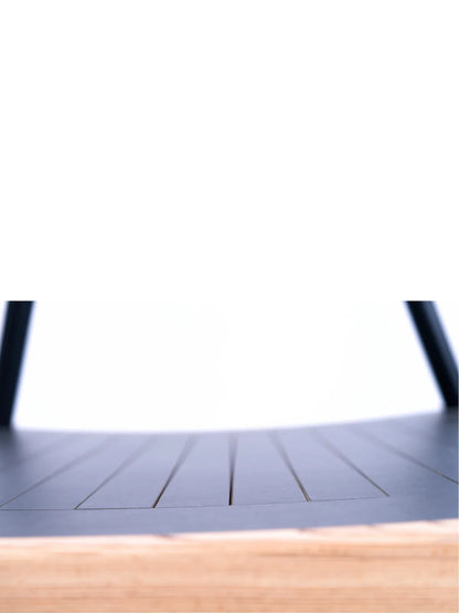 Close-up of the Walkolution 1: a black, curved seat with thin parallel lines and black legs, revealing a light wood layer at the edge. Set against a white background—ideal for pairing with a walking desk.