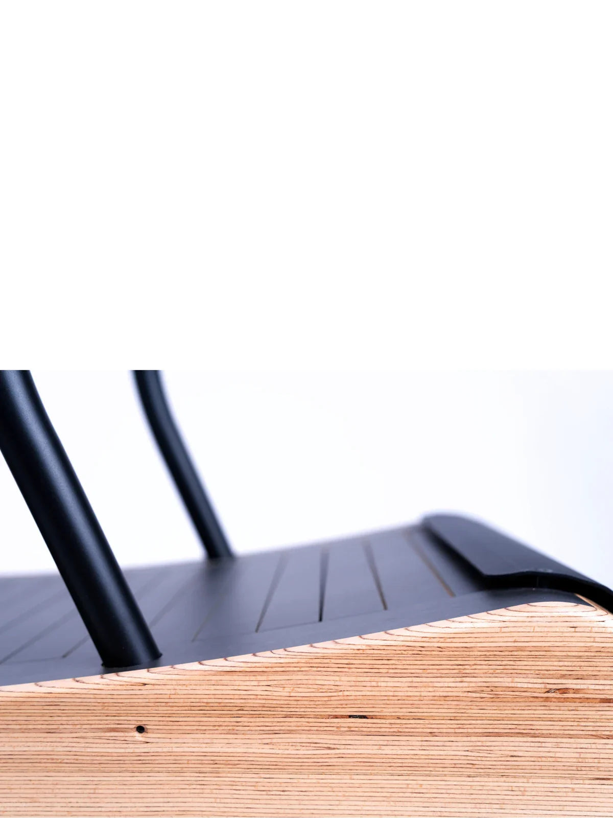 Close-up of a modern chair showing black metal legs and backrest, with a light-colored wooden seat that has visible layered edges and grooves. The background is white and minimalist. Walkolution Global