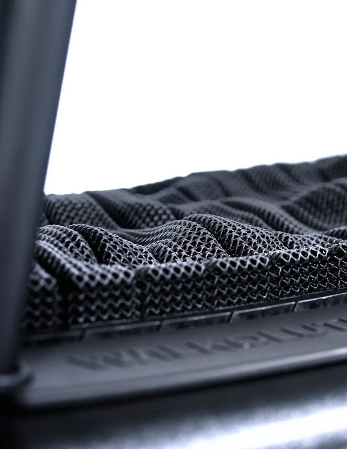 Close-up of the TheraFloor® Home Upgrade-Kit for Walkolution 1, featuring a textured black cushioned mat with a mesh-like pattern and raised wavy ridges. A blurred dark frame appears on the left against a white background.