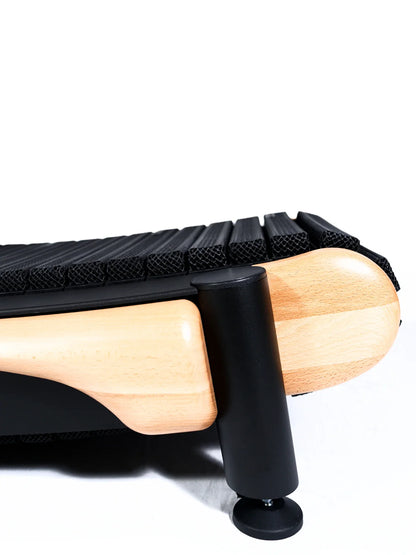 Close-up of the TheraFloor® Home Upgrade-Kit for Walkolution 1: features light wood legs, a black cylindrical support, and a ribbed black cushion resembling a treadmill mat, set against a white background.