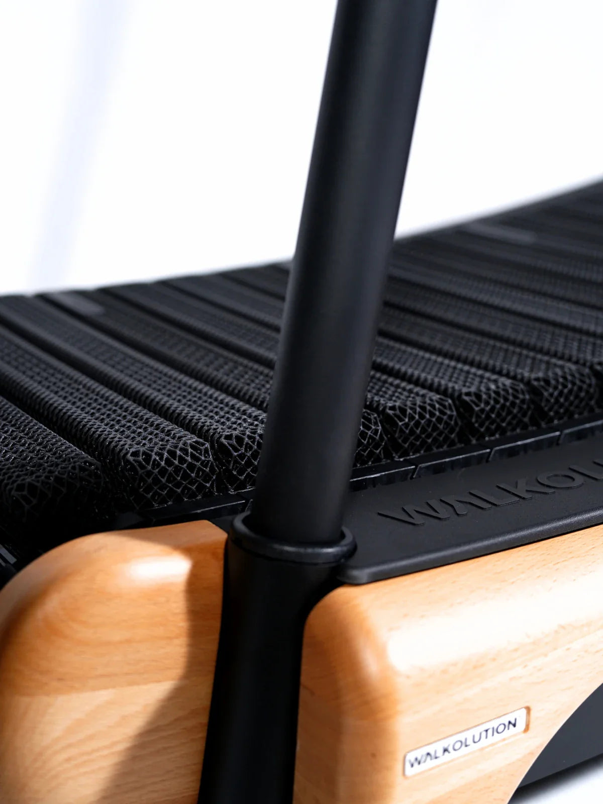 Close-up of a treadmill with a wooden frame and black mesh running surface. The WALKOLUTION logo is visible on the side and base. Two vertical black bars are part of the treadmill structure. Walkolution Global