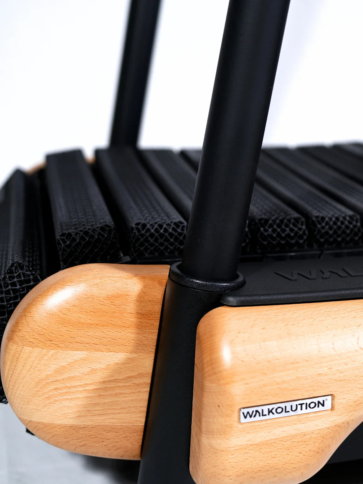Close-up of a Walkolution treadmill, showing black textured treadmill slats, two wooden side panels, and a black metal frame. The Walkolution logo is visible on a wooden panel. Walkolution Global