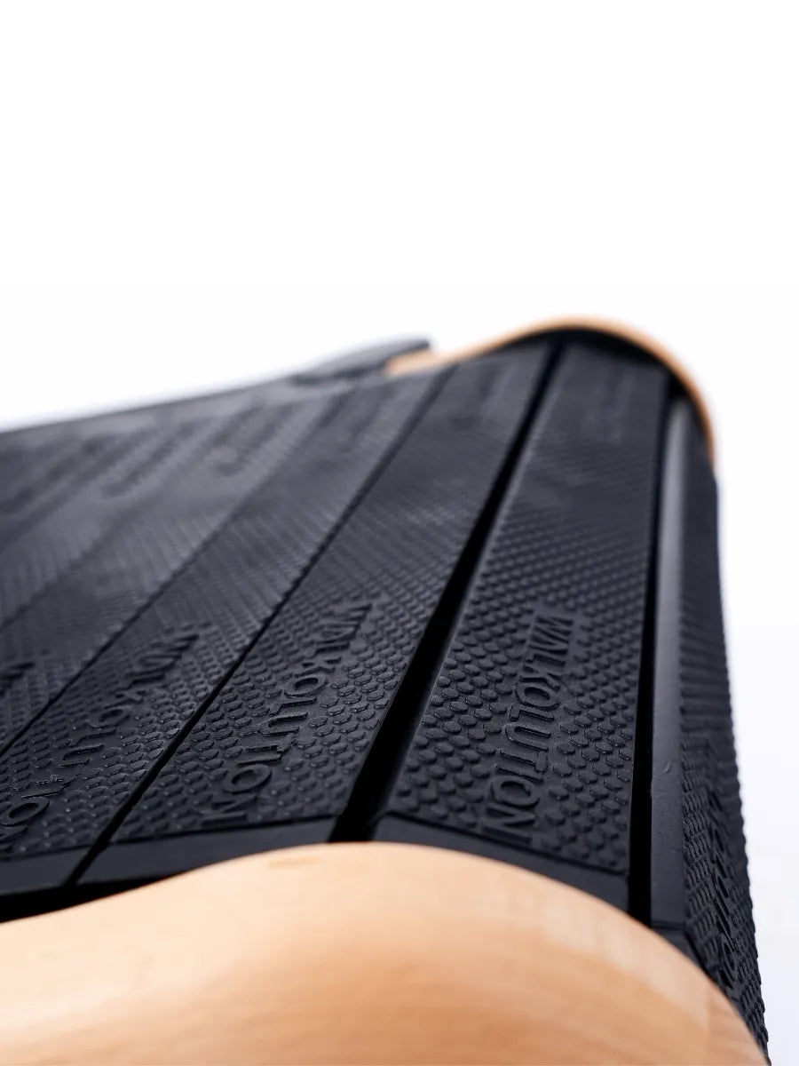 Close-up view of a black textured surface with the word REVOLUTION embossed on it, framed by light-colored wooden edges, likely part of a balance board or fitness equipment. Walkolution Global