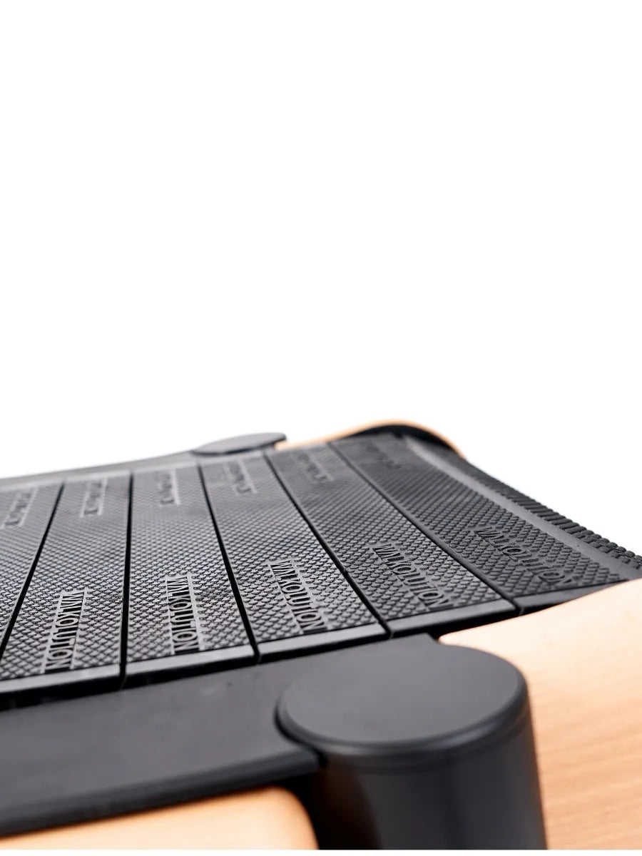 Close-up view of a modern wooden and black Pilates Reformer machine, focusing on the textured black foot platform and part of the frame, against a white background. Walkolution Global