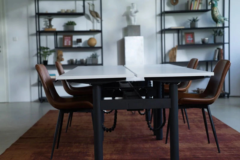 A modern meeting room with two white tables, brown chairs, a red rug, and black shelves displaying books, plants, and decorative items against a white wall. Walkolution Global
