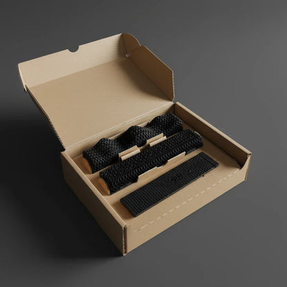The All Surfaces Sample Box is an open cardboard box on a gray surface, holding neatly organized black treadmill surface samples and supports in compartments for barefoot comfort. Its lid is propped open.