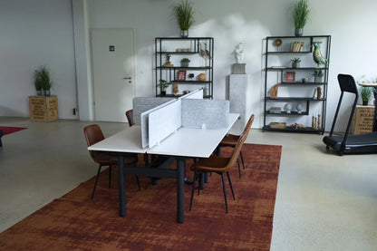 A modern office with the Walkolution Forum Conference Desk, gray privacy panels, brown chairs, open shelving with plants and decor, a treadmill, and a red area rug on a light floor.