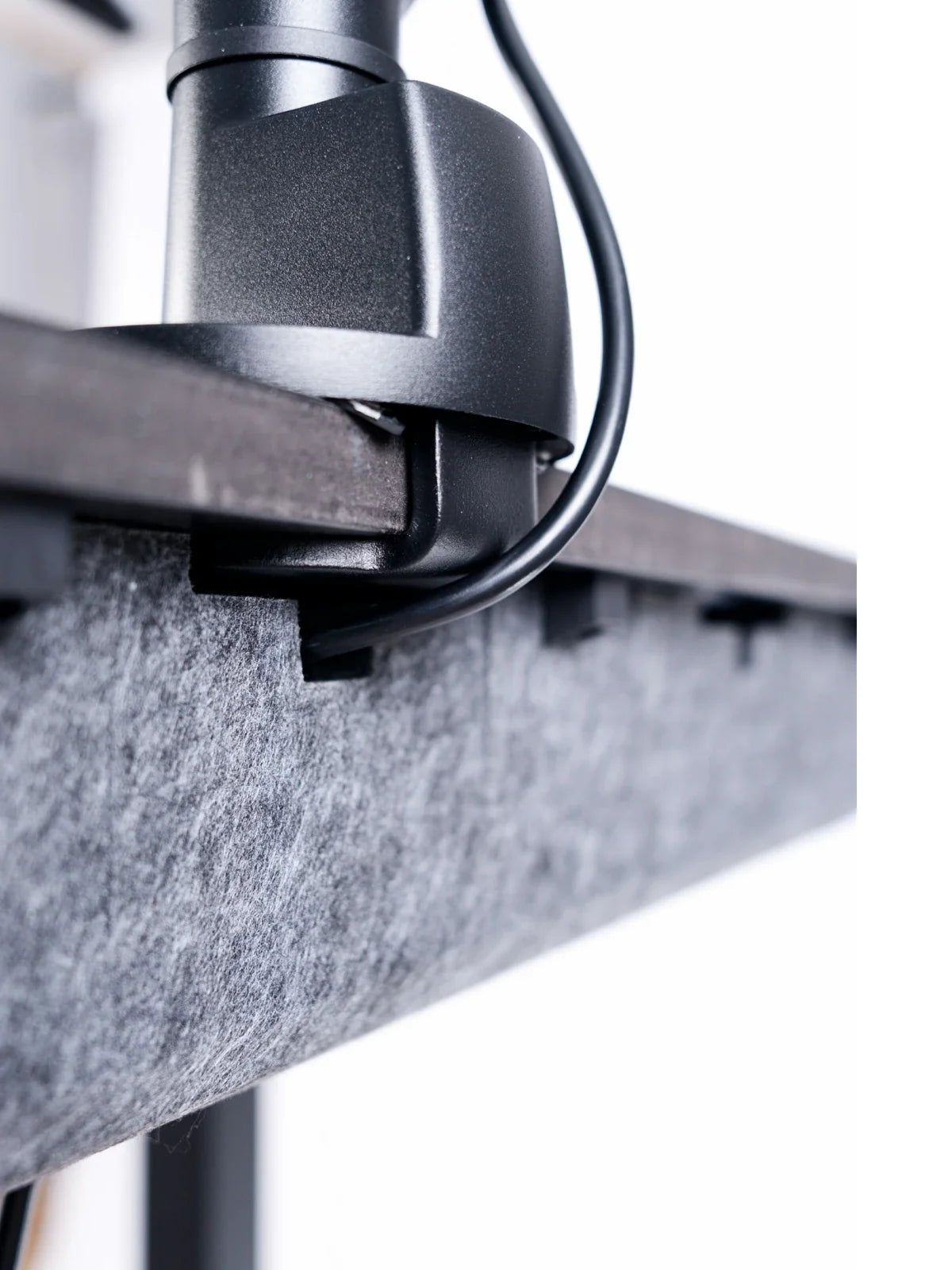 A Walkolution Pro Desk Cable Organizer in eco-friendly gray felt is attached under a dark wooden desk, while a clamp secures a black monitor arm to the edge, keeping the workspace neat and organized.