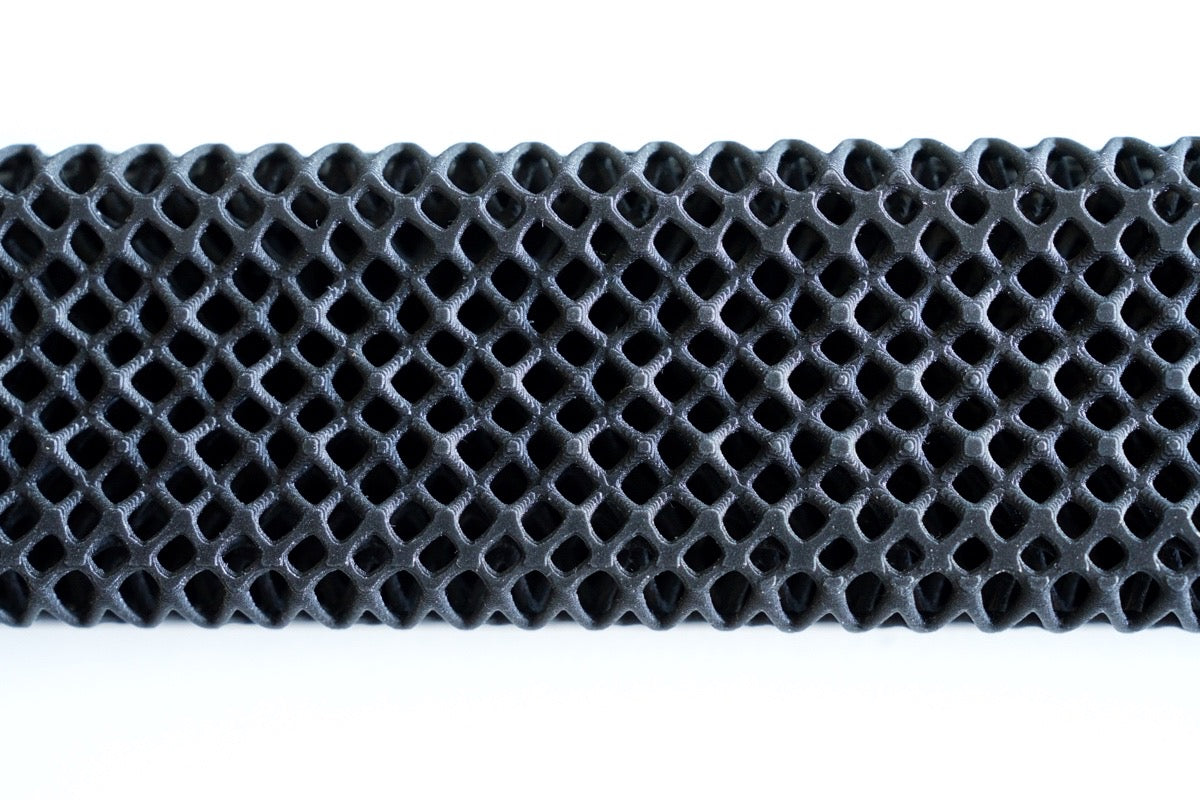 A close-up of a black, honeycomb-patterned lattice structure highlights the barefoot comfort provided by the All Surfaces Sample Box treadmill surface samples, set against a white background.