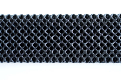 A close-up of a black, honeycomb-patterned lattice structure highlights the barefoot comfort provided by the All Surfaces Sample Box treadmill surface samples, set against a white background.