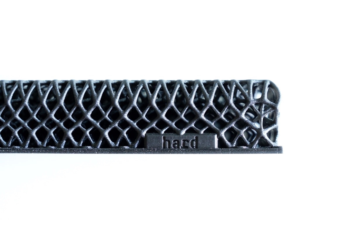 A close-up of a black, lattice-like 3D-printed structure labeled "hard," from the All Surfaces Sample Box, showcasing one treadmill surface sample against a white background.