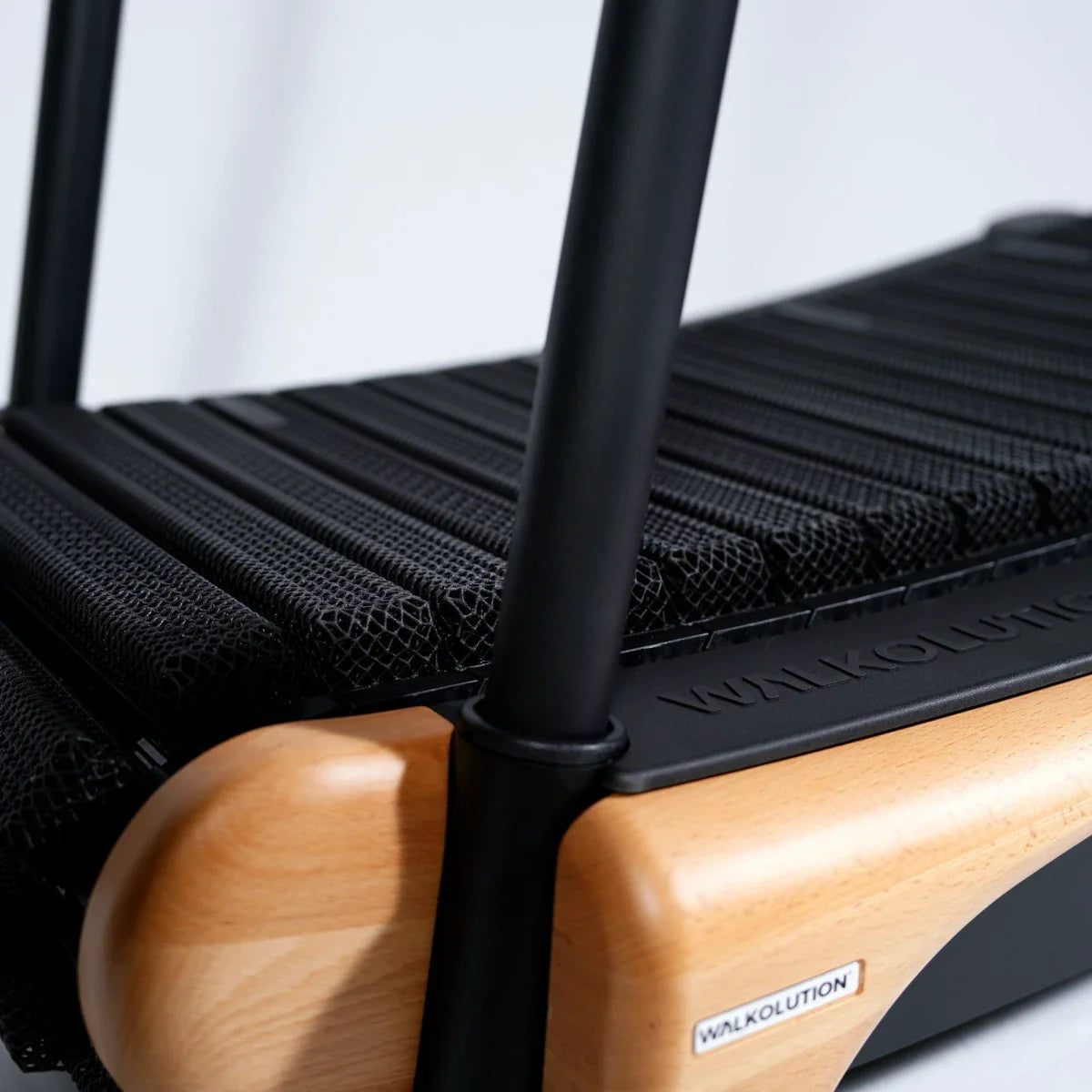 Close-up of a modern treadmill with a wooden frame, black mesh running surface, and sturdy black metal handles. The brand name WALKOLUTION is visible on a label and engraved on the side.