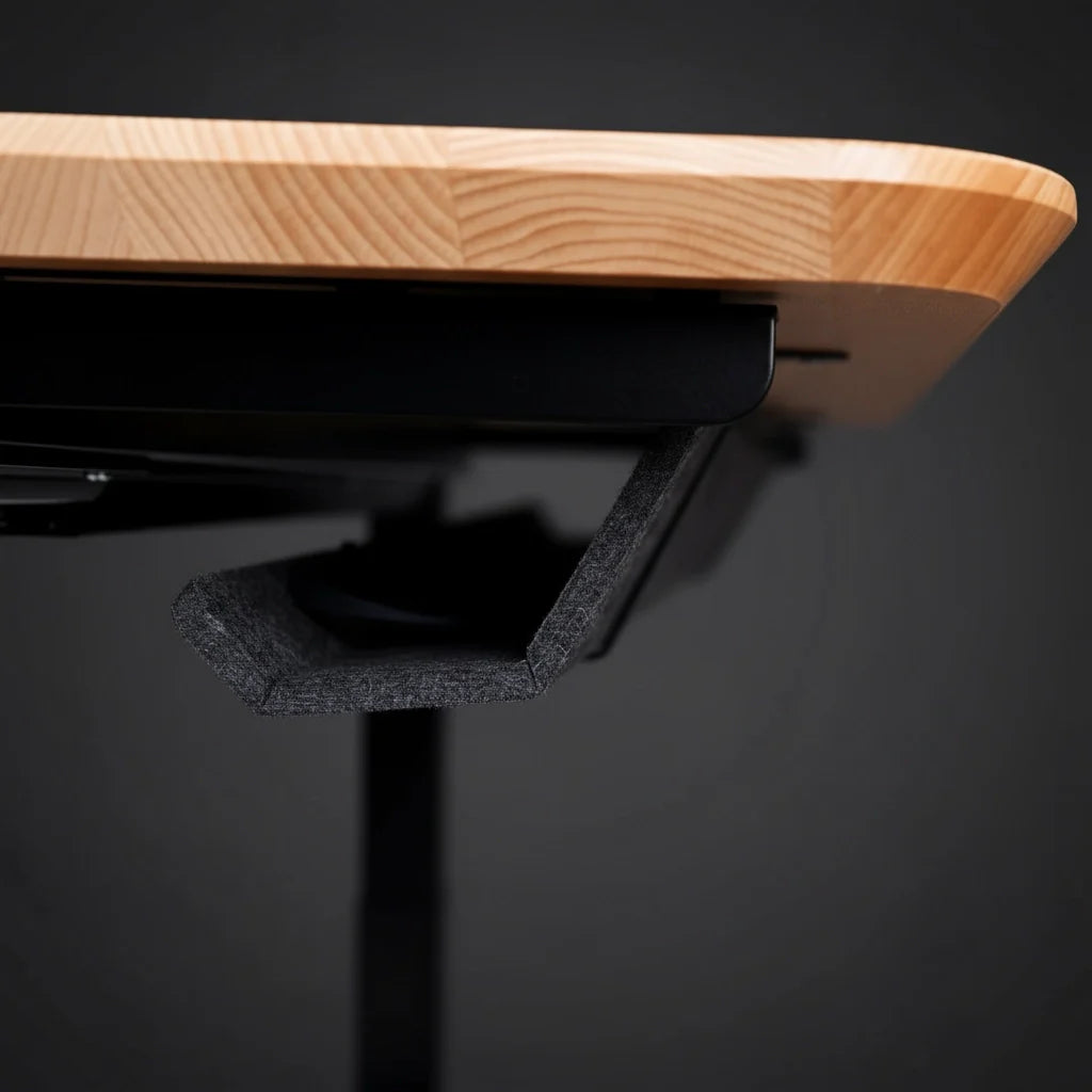 A close-up view of the underside of a wooden desk, featuring a black, angular foam cable management tray attached to the desks edge, against a dark background. Walkolution Global