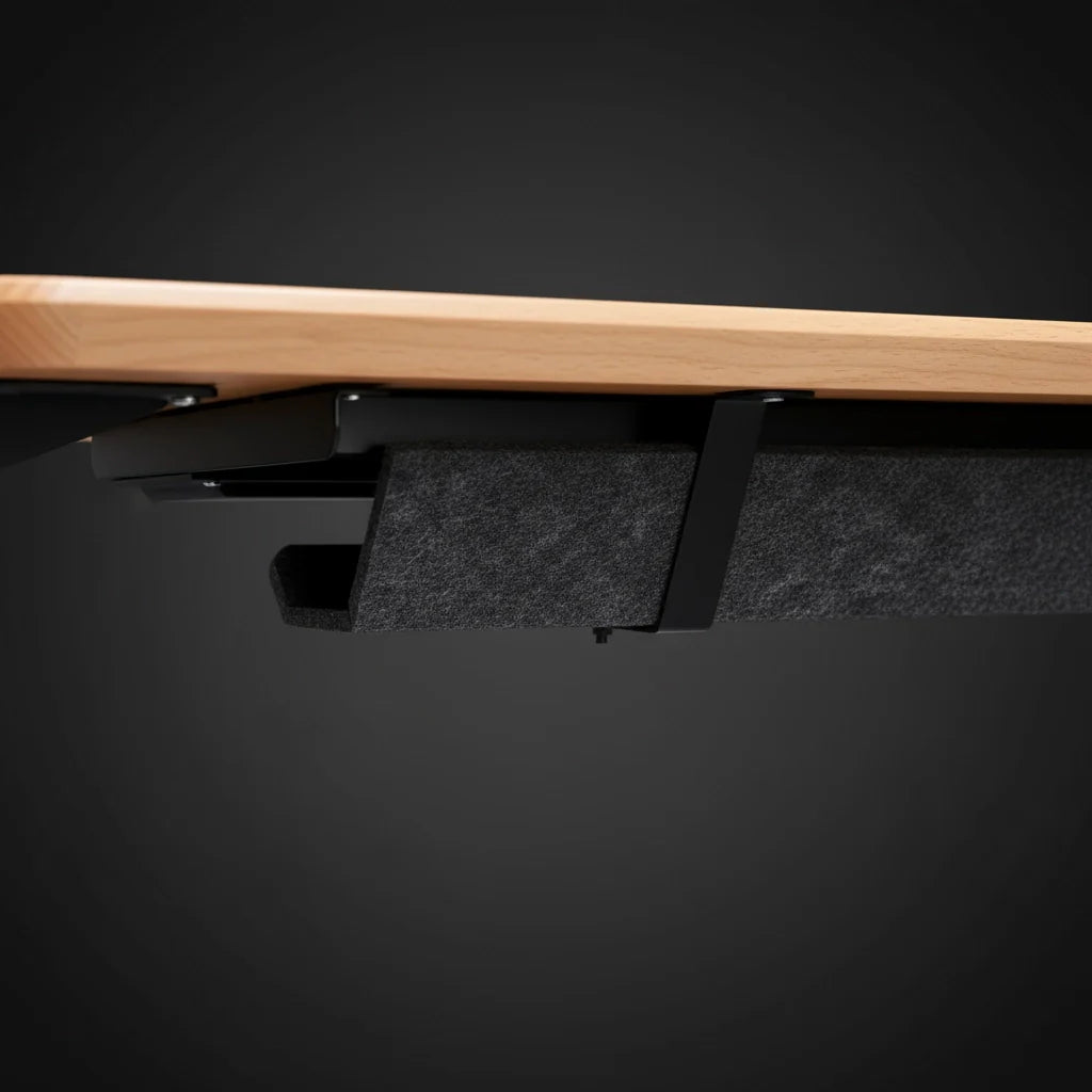 A close-up side view of the underside of a wooden desk, showing a black felt cable management tray attached underneath, with a sleek and minimal design against a dark background. Walkolution Global